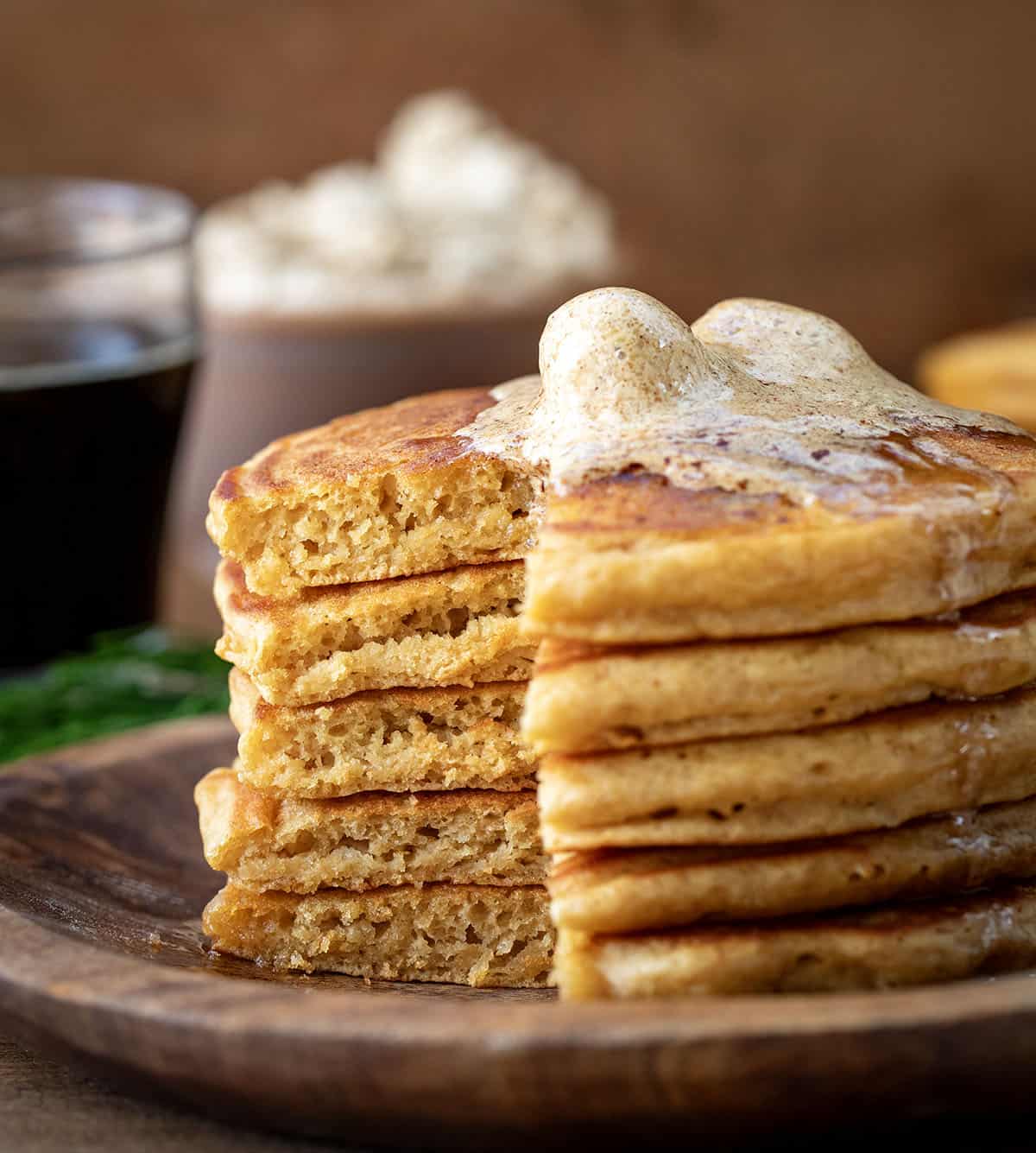 Stack of cut into Gingerbread Pancakes on a wooden plate with whipped gingerbread butter on top.