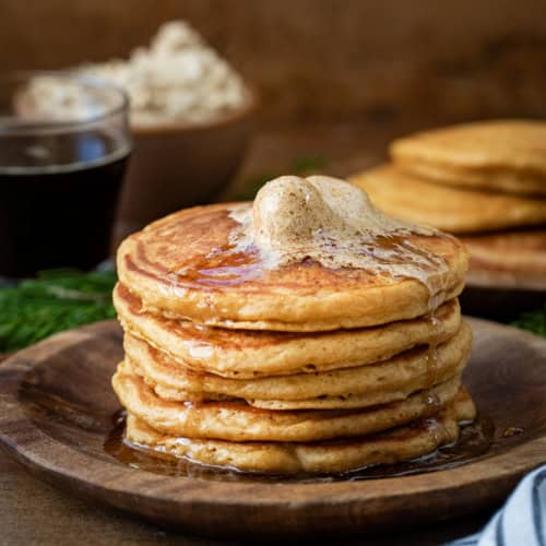 Stack of Gingerbread Pancakes on a wooden plate with gingerbread butter on top.