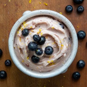 Looking at a cup of Lemon Blueberry Butter with blueberries on top on a wooden table.