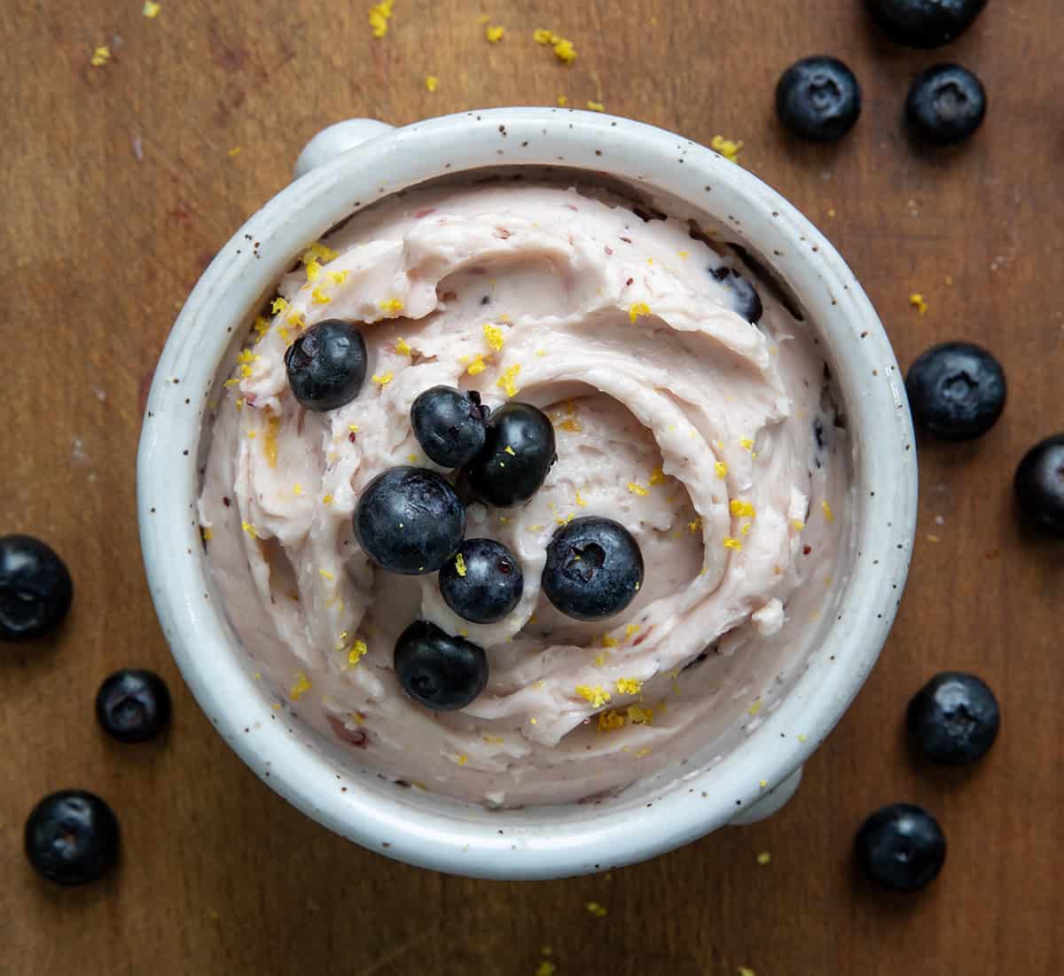 Looking at a cup of Lemon Blueberry Butter with blueberries on top on a wooden table.