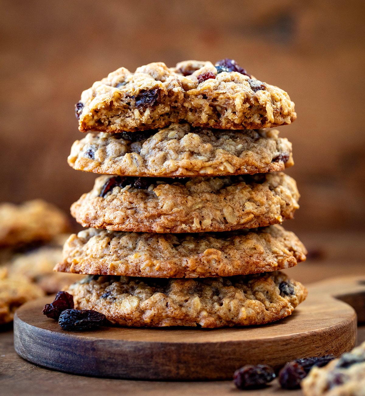 Stack of Cookies with top cookie broken in half showing soft texture of Oatmeal Raisin Cookies.