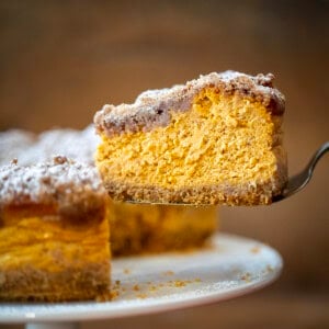 Spatula holding a piece of Pumpkin Crumble Cheesecake near the cake stand.