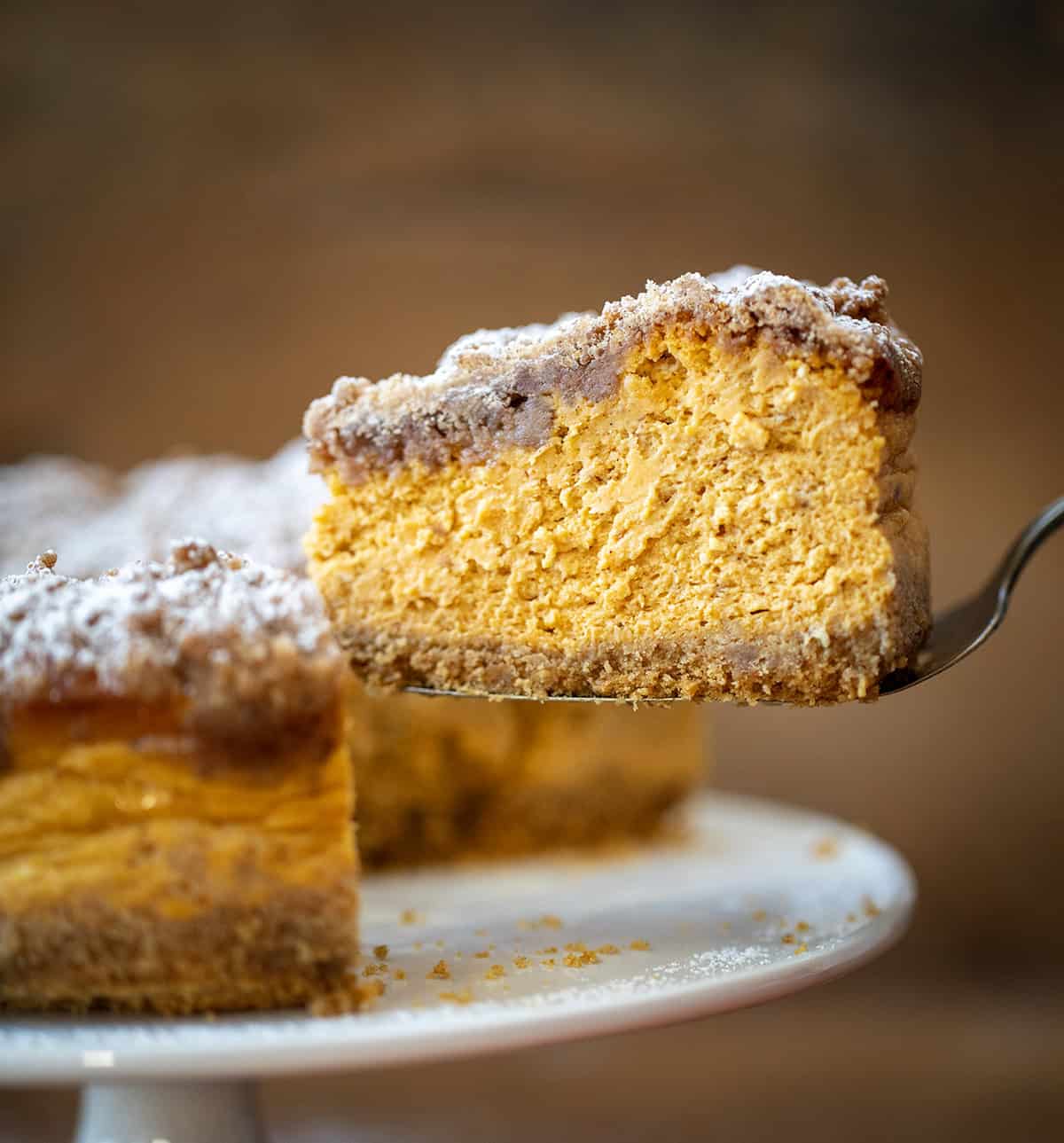 Spatula holding a piece of Pumpkin Crumble Cheesecake near the cake stand.