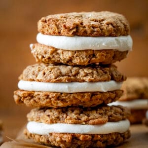 Stack of Pumpkin Oatmeal Cream Pie cookies on a cutting board on a wooden table.