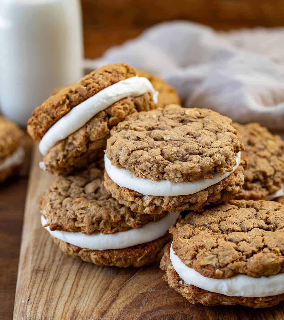 Pumpkin Oatmeal Cream Pies arranged on a cutting board with milk and a towel in the background.