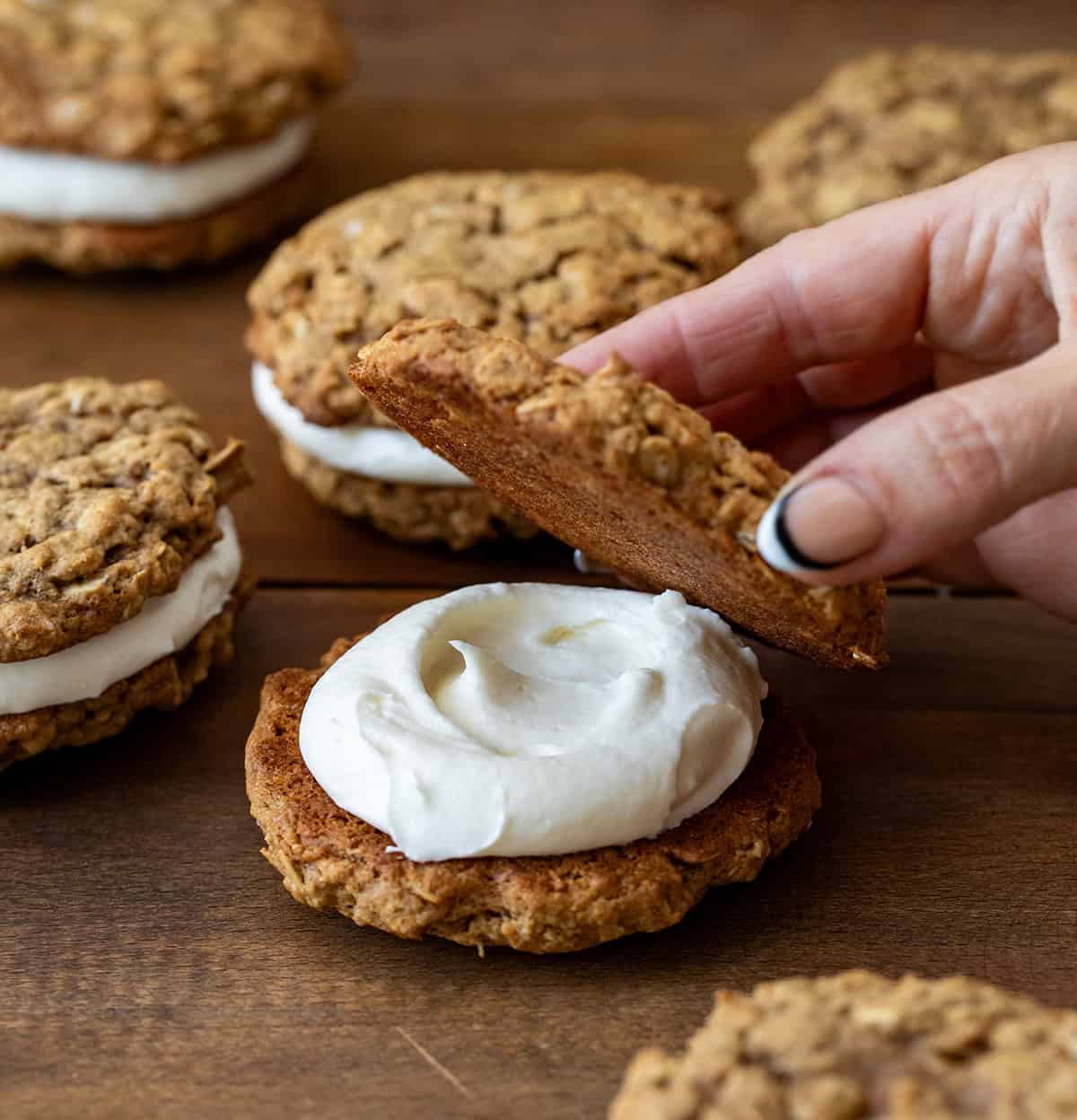 Placing a pumpkin oatmeal cookie on top of marshmallow frosting to make a Pumpkin Oatmeal Cream Pie.