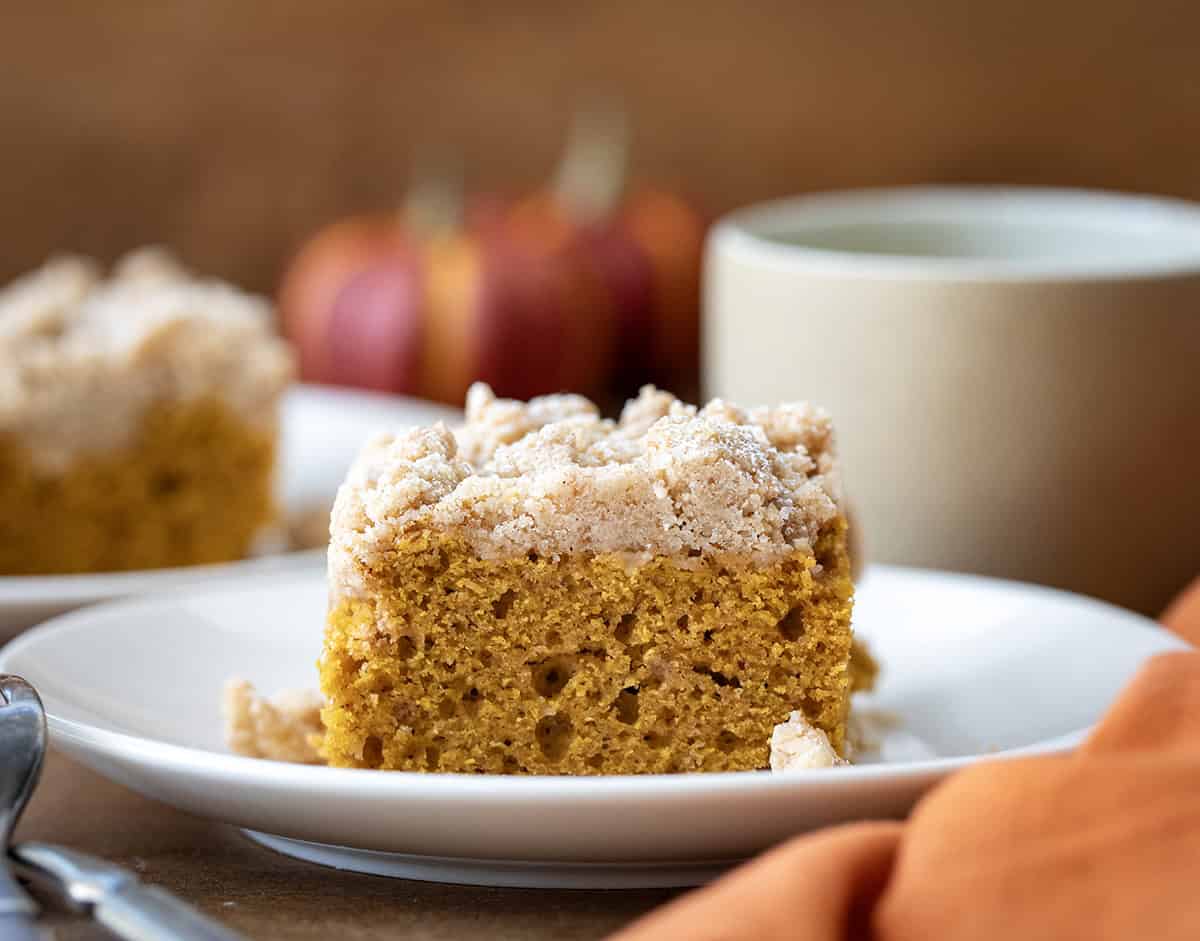 Slice of Pumpkin Spice Coffee Cake on a white plate on a wooden table with coffee.