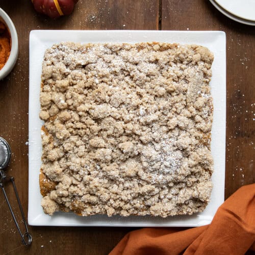 Whole Pumpkin Spice Coffee Cake on a white platter on a wooden table from overhead.