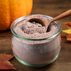 Wooden tablespoon in a jar of Pumpkin Spice Hot Cocoa Mix on a wooden table.