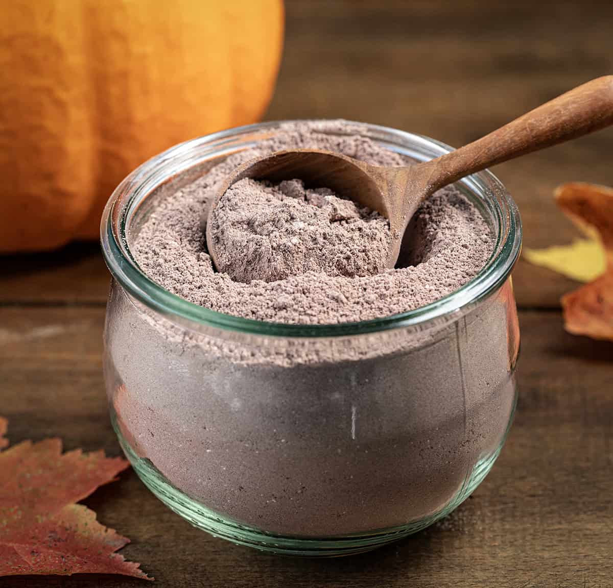 Wooden tablespoon in a jar of Pumpkin Spice Hot Cocoa Mix on a wooden table.