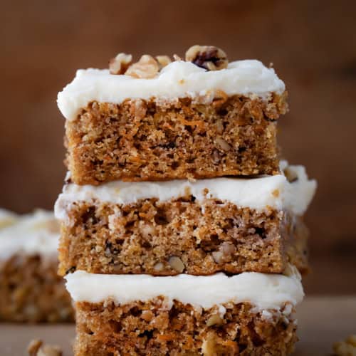 Stack of Sheet Pan Carrot Cake Bars on a wooden table.