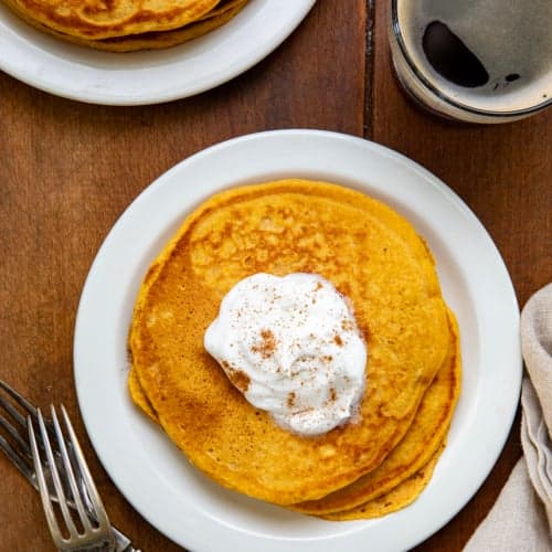 White plates on a wooden table with Sweet Potato Pancakes on them from overhead.