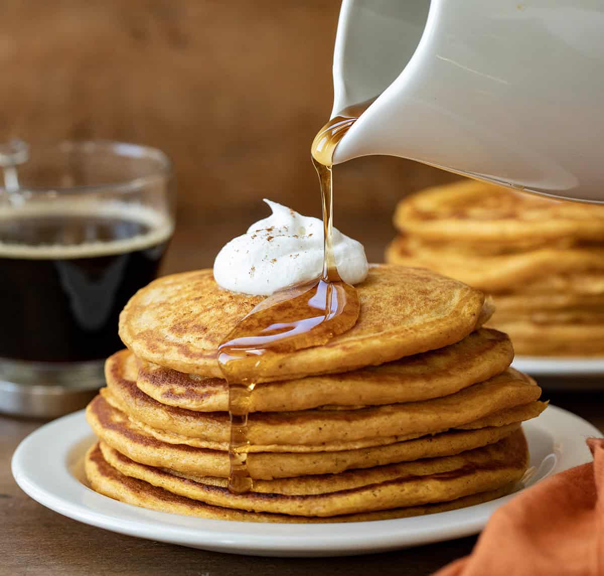 Drizzling syrup over Sweet Potato Pancakes on a white plate on a wooden table. 