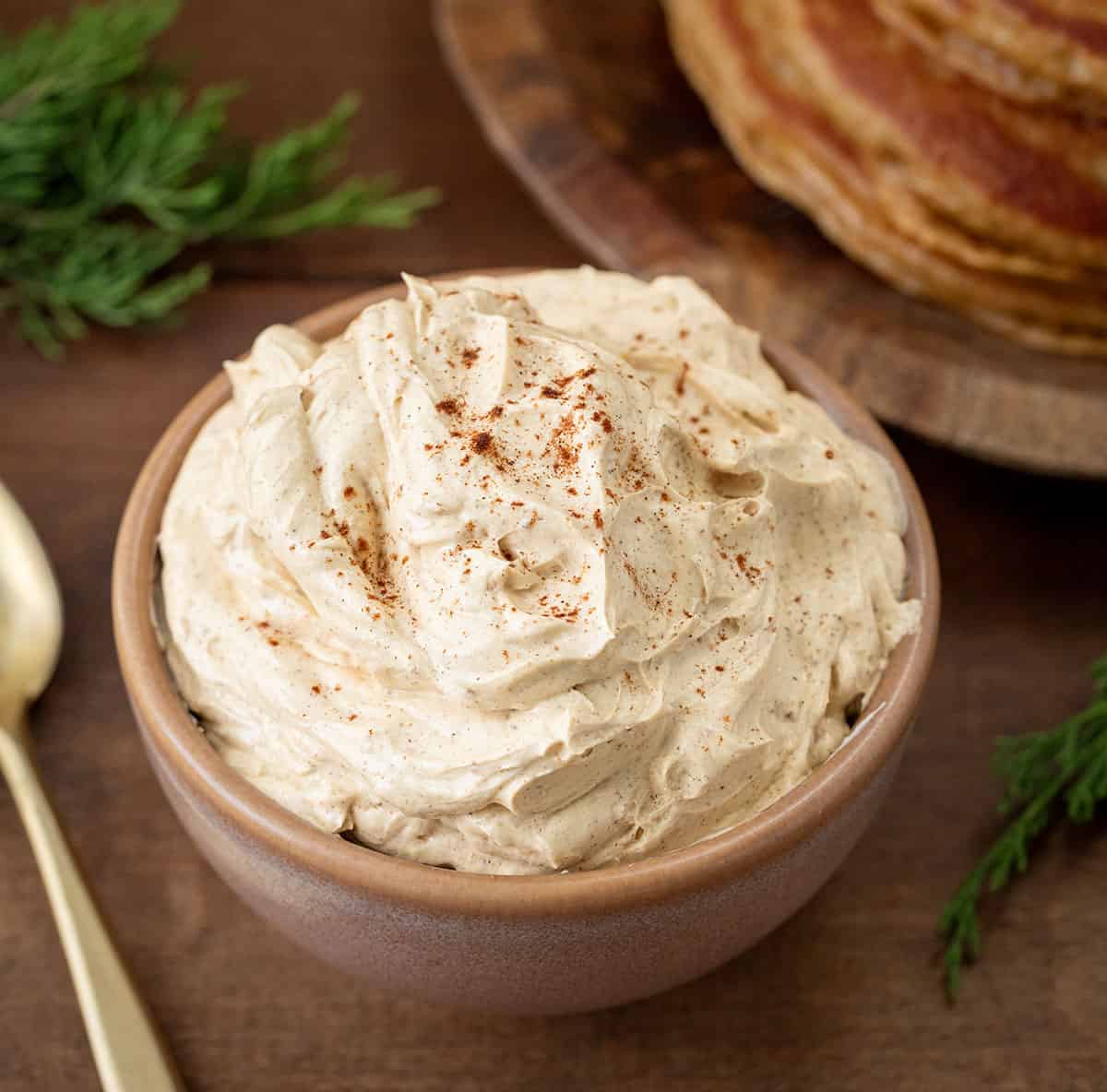 Bowl of Whipped Gingerbread Butter on a wooden table near gingerbread pancakes.