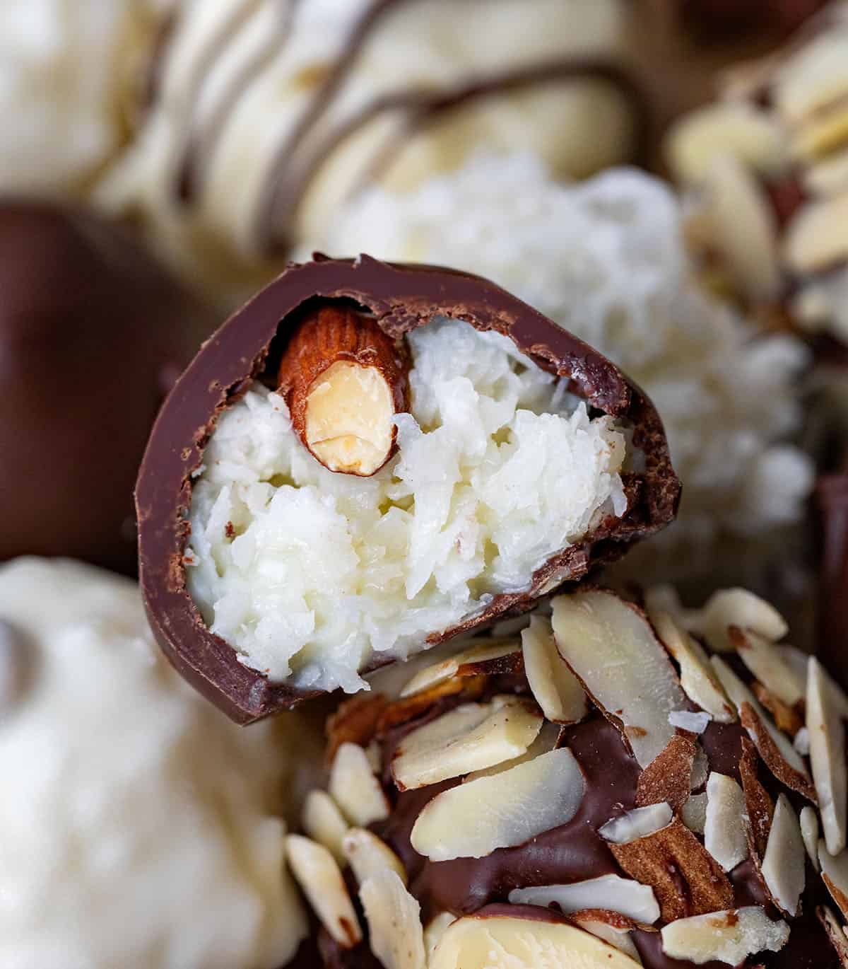 One Almond Joy Truffle cut in half showing inside filling and sitting on top of other truffles.