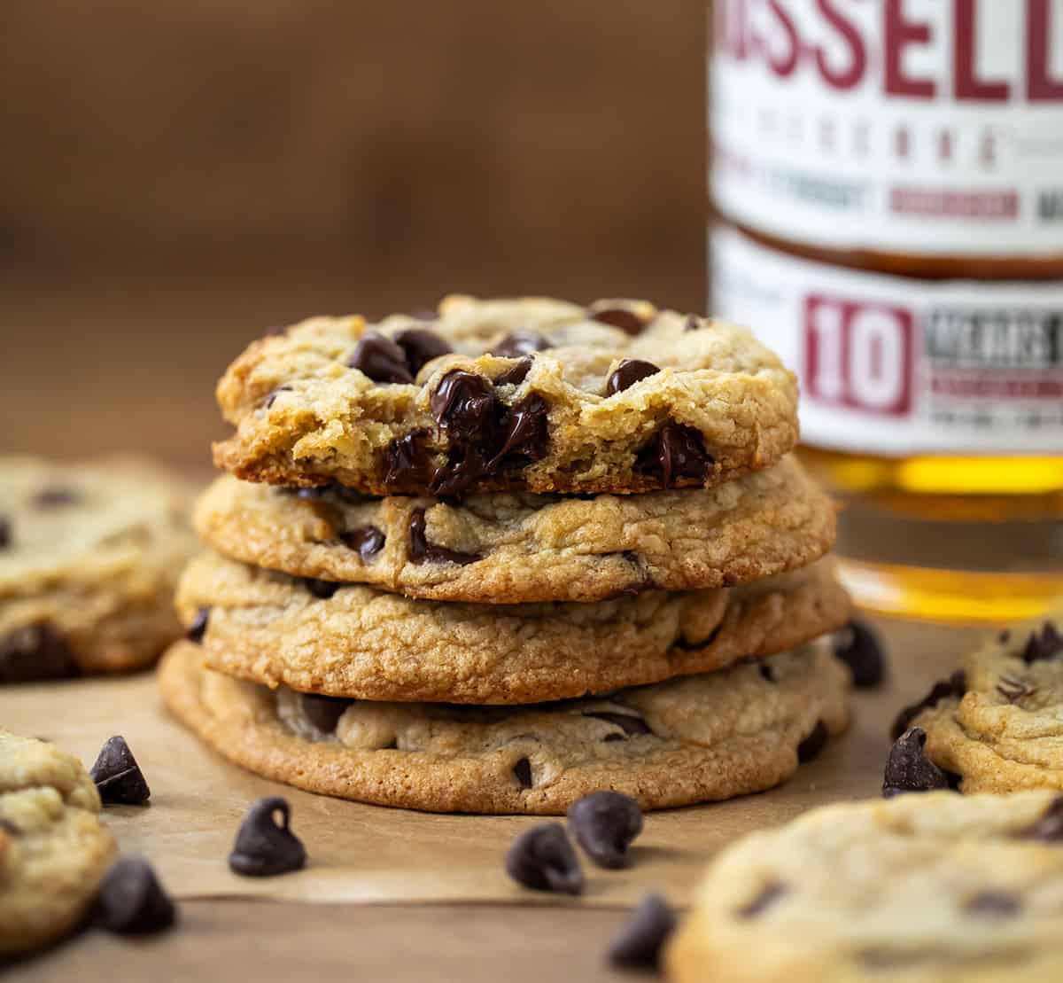 Stack of Bourbon Browned Butter Chocolate Chip Cookies with the top cookie broken in half and all in front of a bourbon bottle.