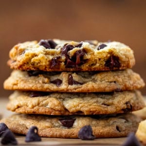 Stack of Bourbon Browned Butter Chocolate Chip Cookies on a wooden table with top cookie broken in half.