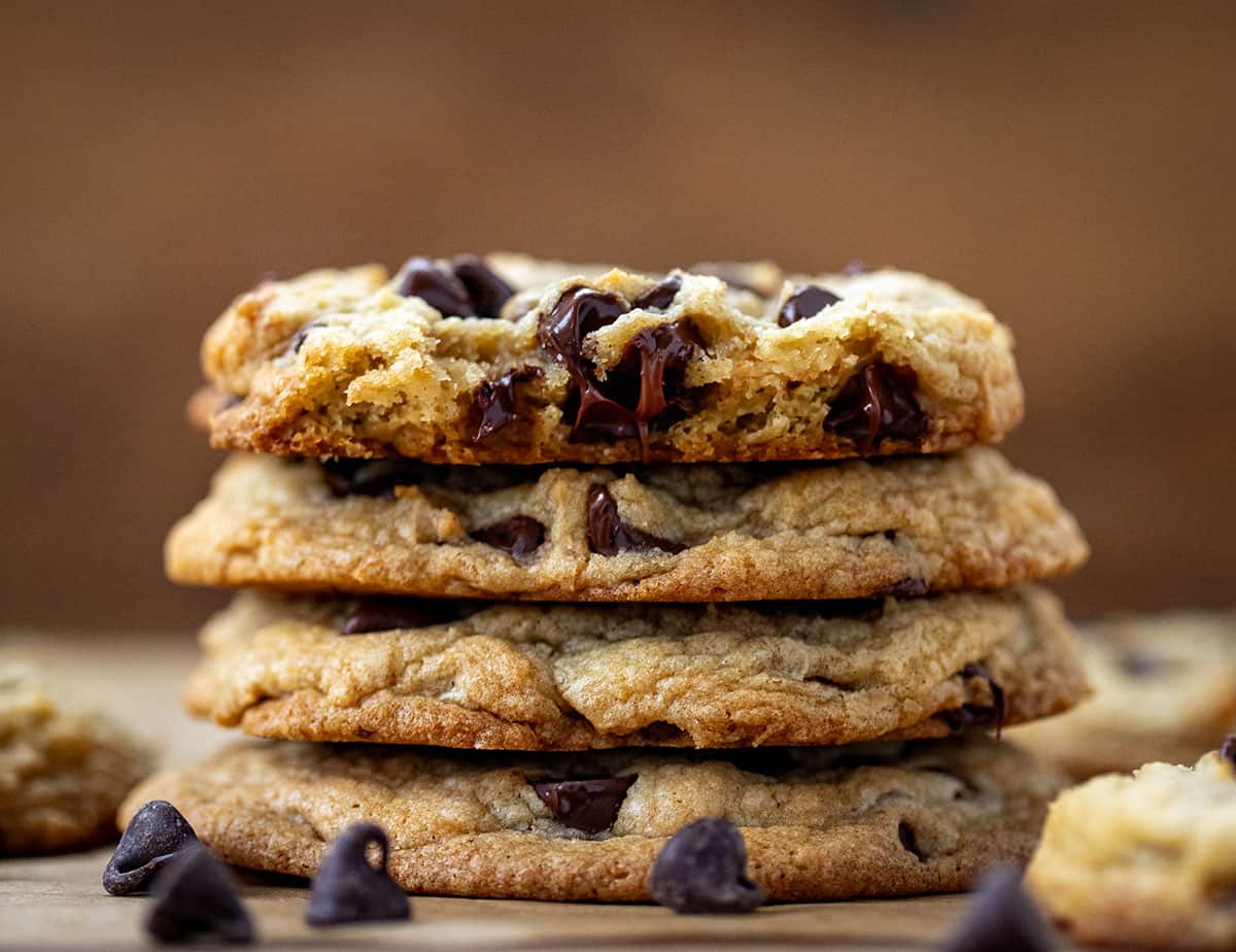 Stack of Bourbon Browned Butter Chocolate Chip Cookies on a wooden table with top cookie broken in half.