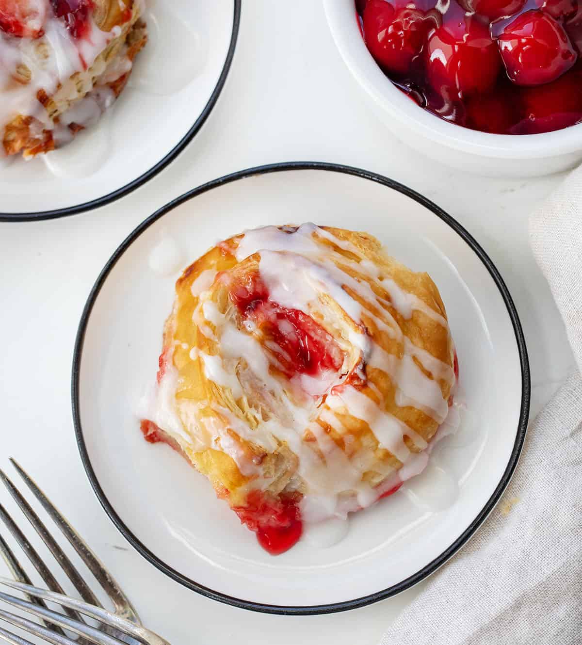 Individual Cherry Cheesecake Pinwheels on white plates on a white table from overhead.