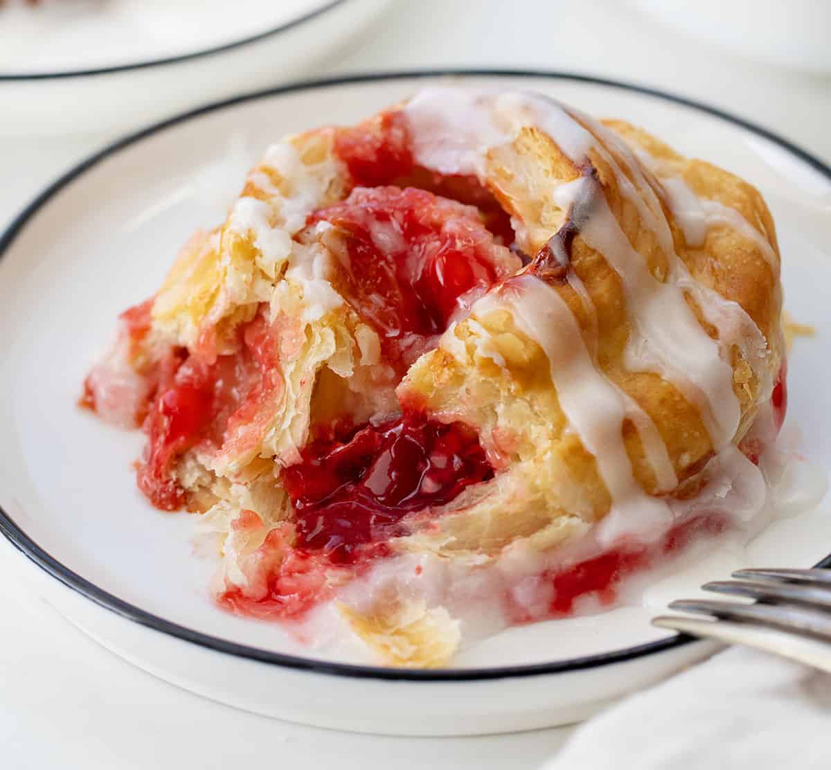 Bit into Cherry Cheesecake Pinwheel on a plate with fork resting on the plate.