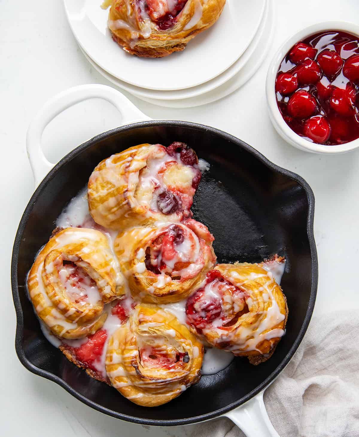 Skillet of Cherry Cheesecake Pinwheels on a white table with one roll removed and sitting in a plate.