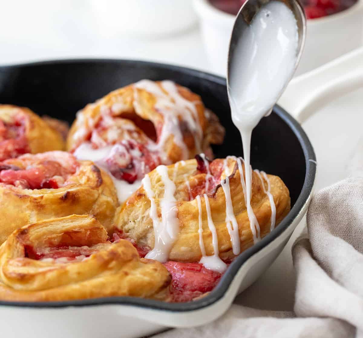 Drizzling glaze over Cherry Cheesecake Pinwheels in a skillet.