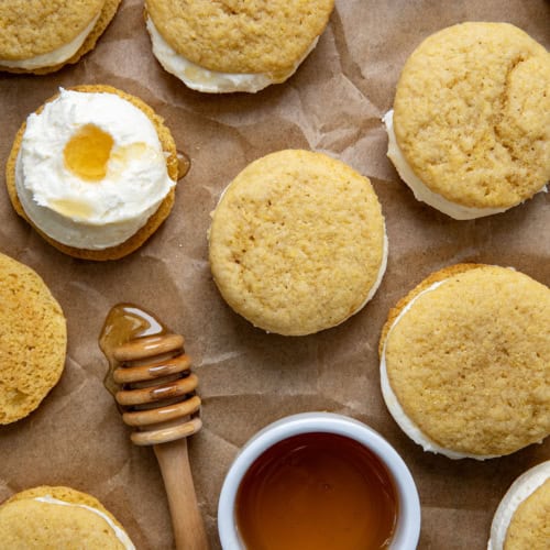 Many Cornbread Sandwich Cookies on a piece of parchment paper and honey from overhead.