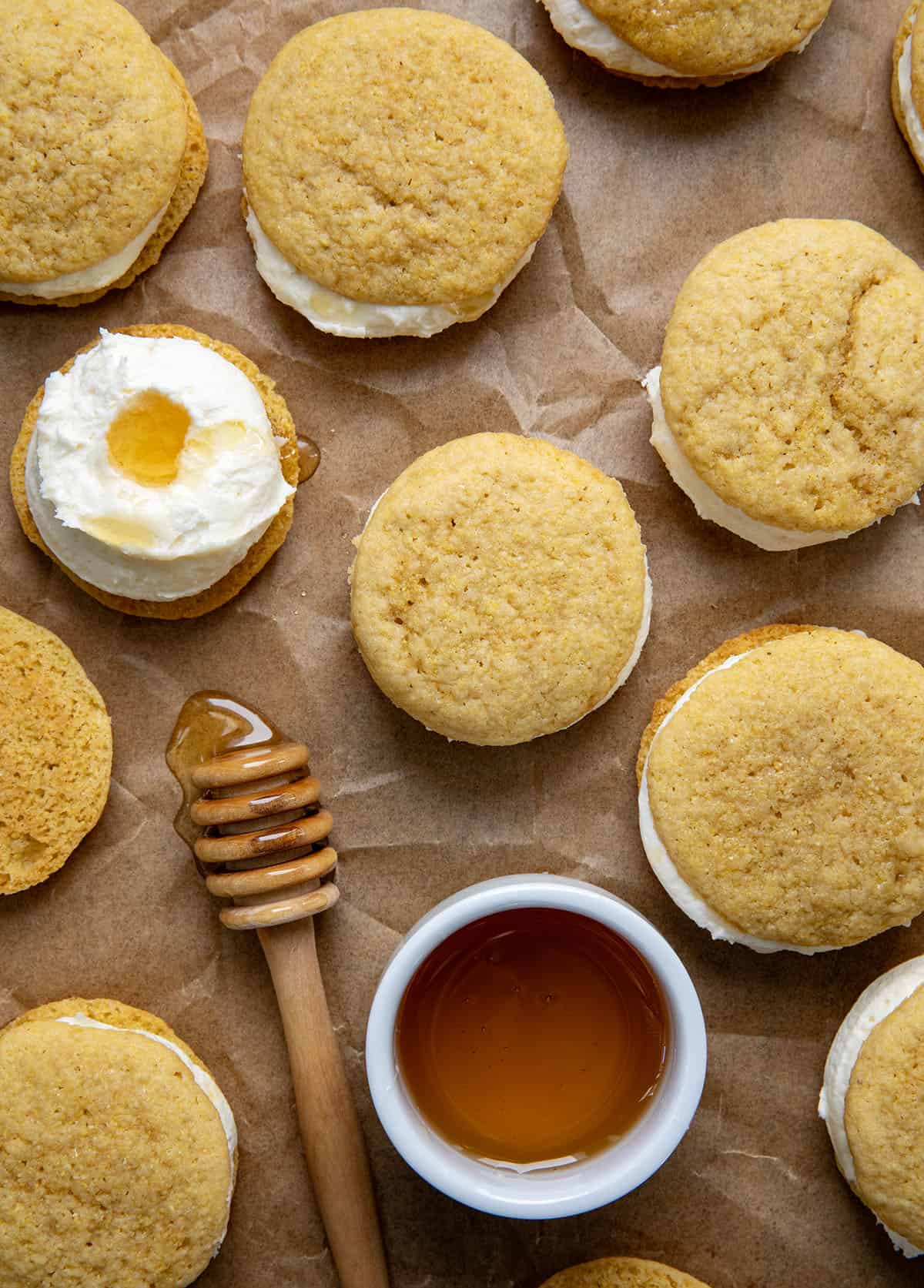 Many Cornbread Sandwich Cookies on a piece of parchment paper and honey from overhead.