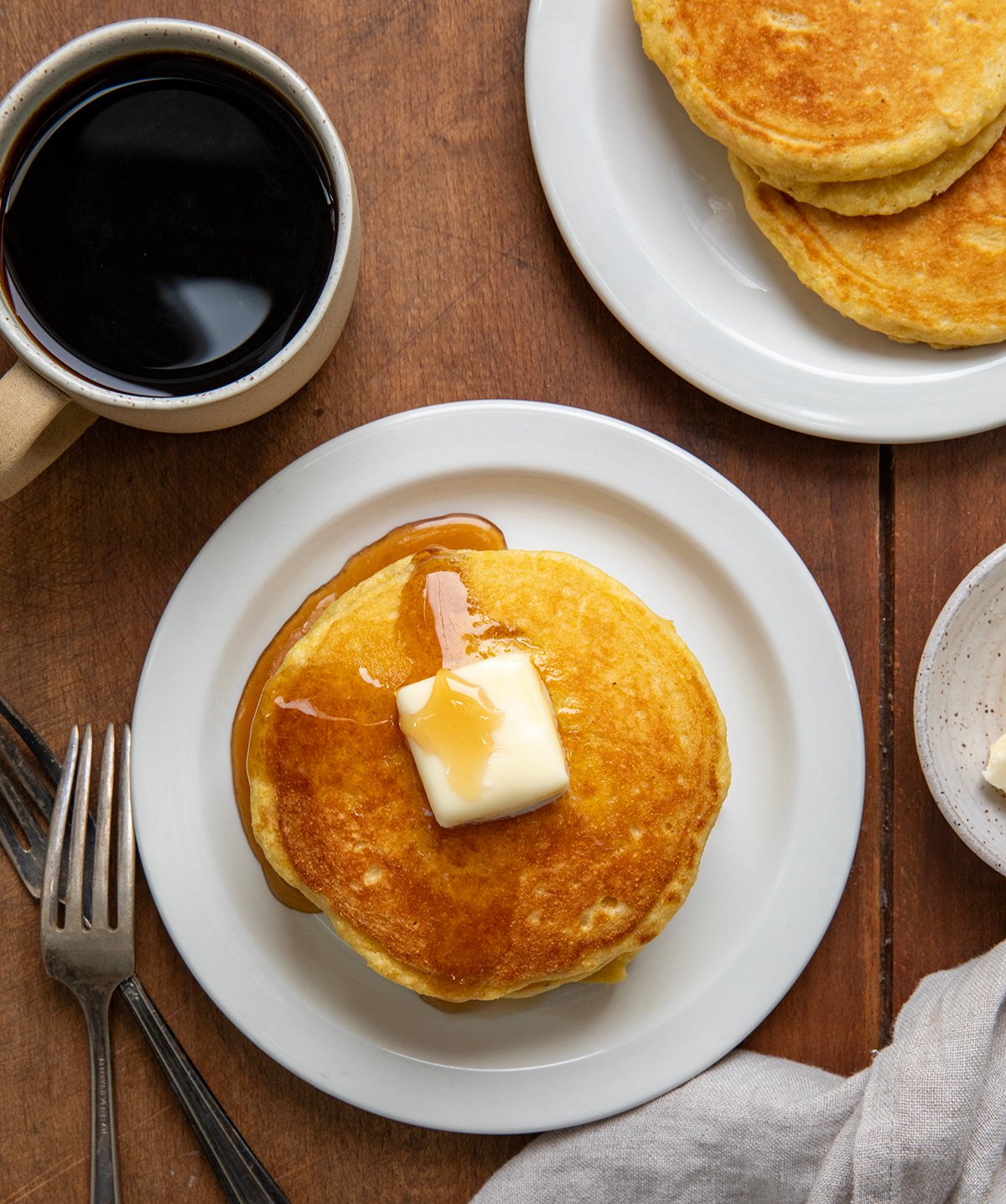 Stacks of Cornmeal Pancakes on white plates on a wooden table from overhead.