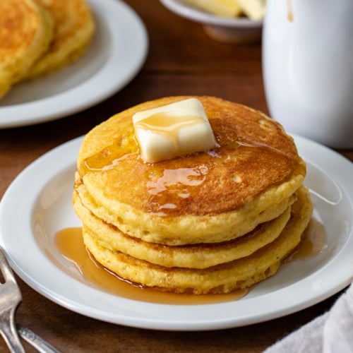 Sack of Cornmeal Pancakes with butter on a white plate.