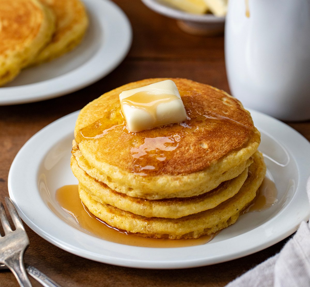 Sack of Cornmeal Pancakes with butter on a white plate.