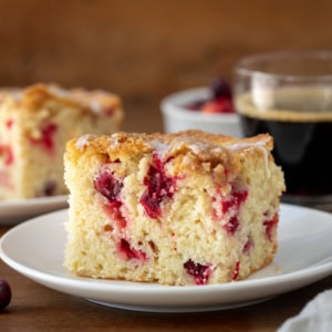 Piece of Cranberry Coffee Cake on a white plate on a wooden table.