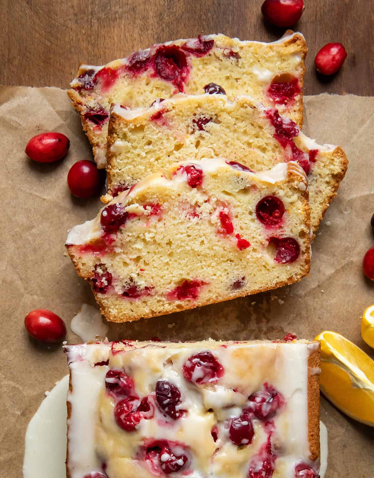 Loaf of Cranberry Orange bread on a wooden table from overhead with a few pieces cut and laying flat.