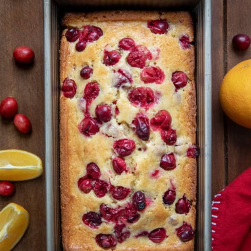 Loaf of Cranberry Orange bread in a pan on a wooden table from overhead.