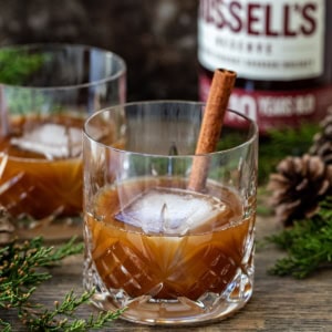 Glasses of Gingerbread Old Fashioned on a table with alcohol in the background.