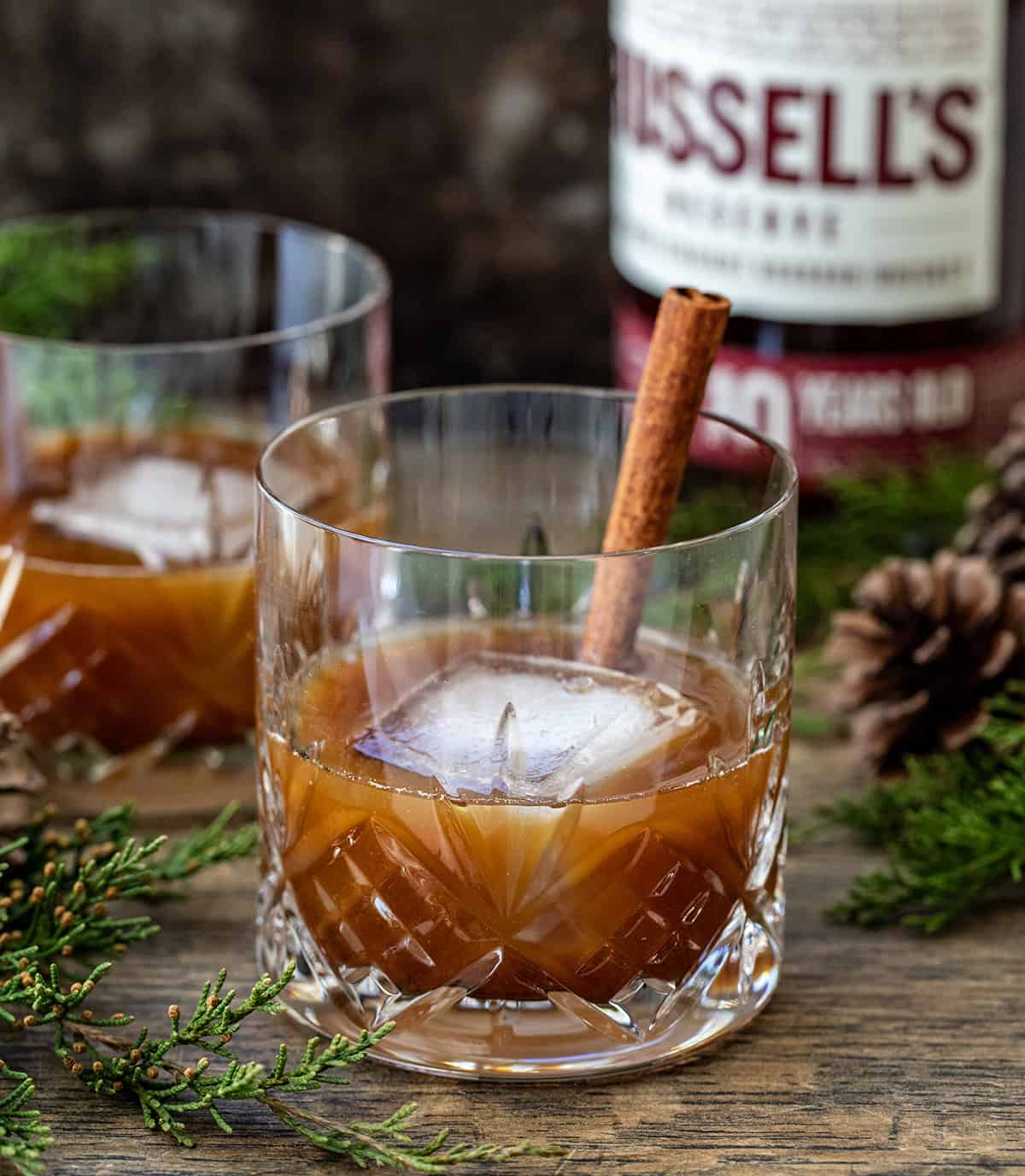 Glasses of Gingerbread Old Fashioned on a table with alcohol in the background.