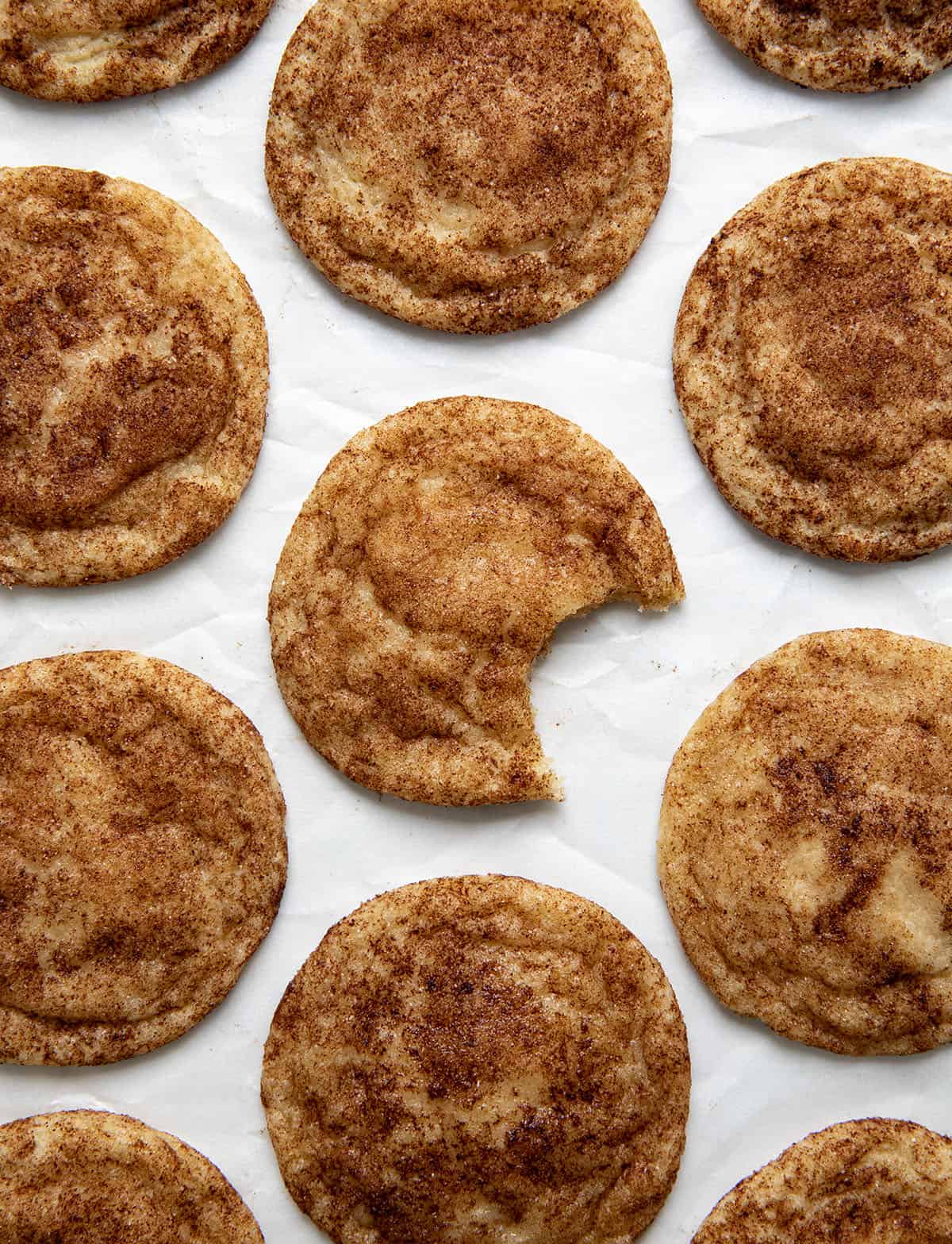 Maple Snickerdoodles on a white piece of parchment paper with the center cookie with a bite taken out of it.