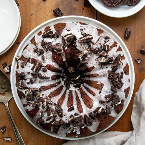 Oreo Bundt Cake on a white cake plate on a wooden table from overhead.