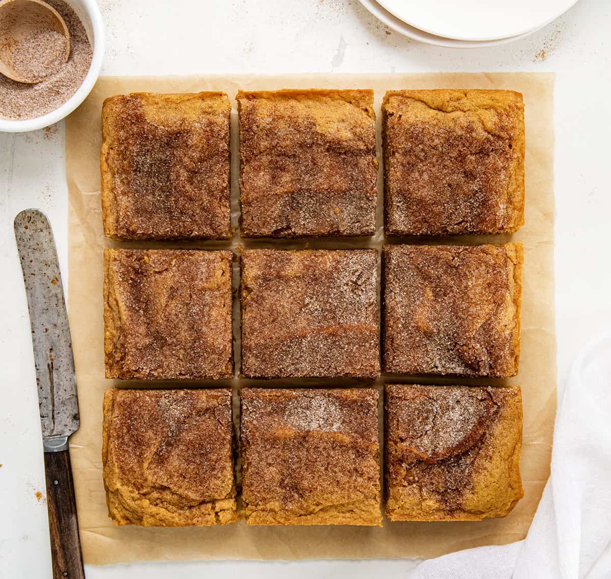 Pumpkin Snickerdoodle Brownies on a white table with cinnamon sugar and a knife from overhead.