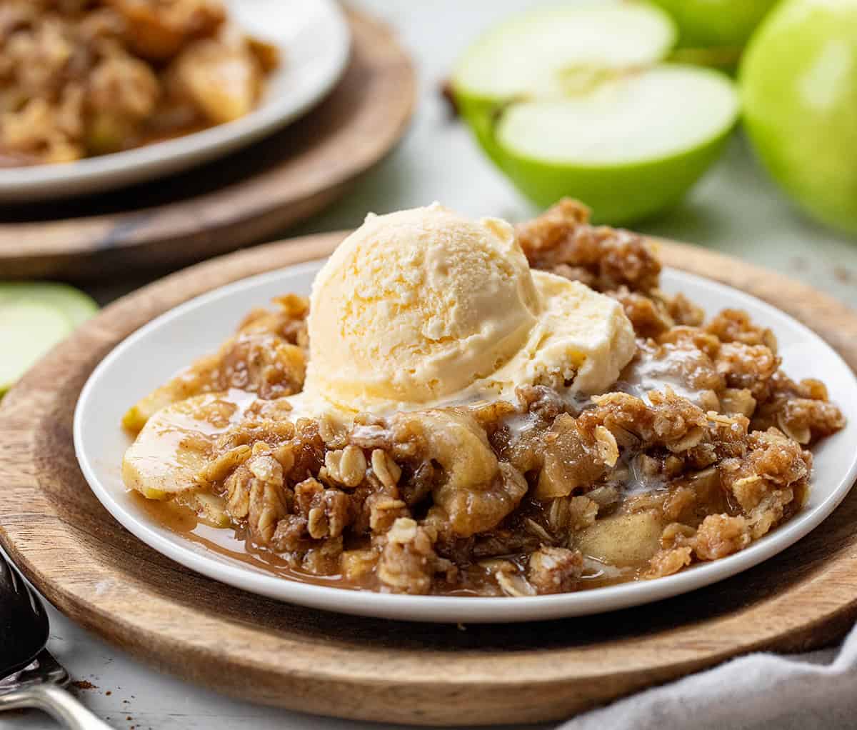 Plates of Slow Cooker Apple Crisp on a white table with cinnamon sticks and apples.