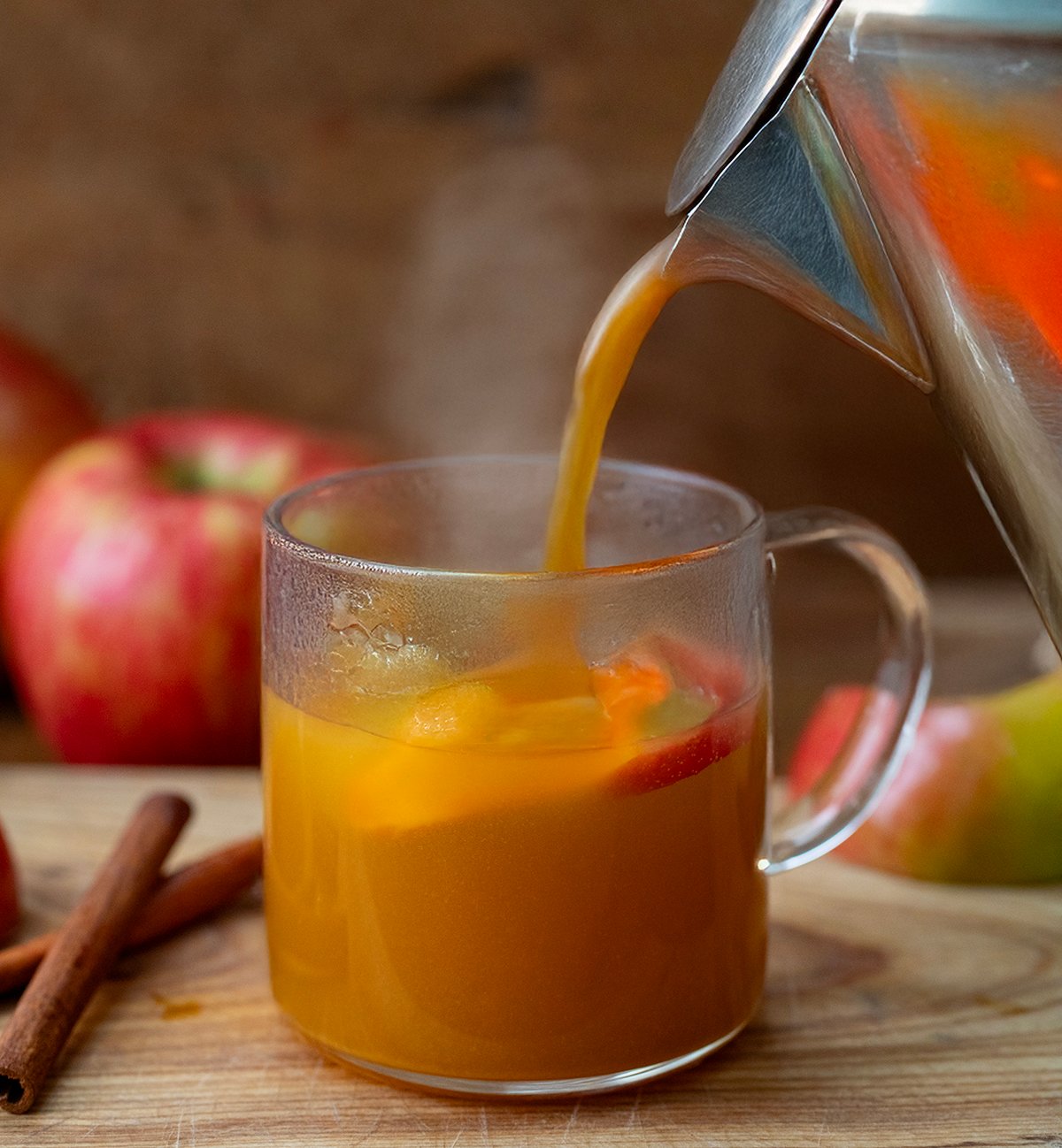 Pouring Spiked Apple Cider into a glass with apples and oranges.