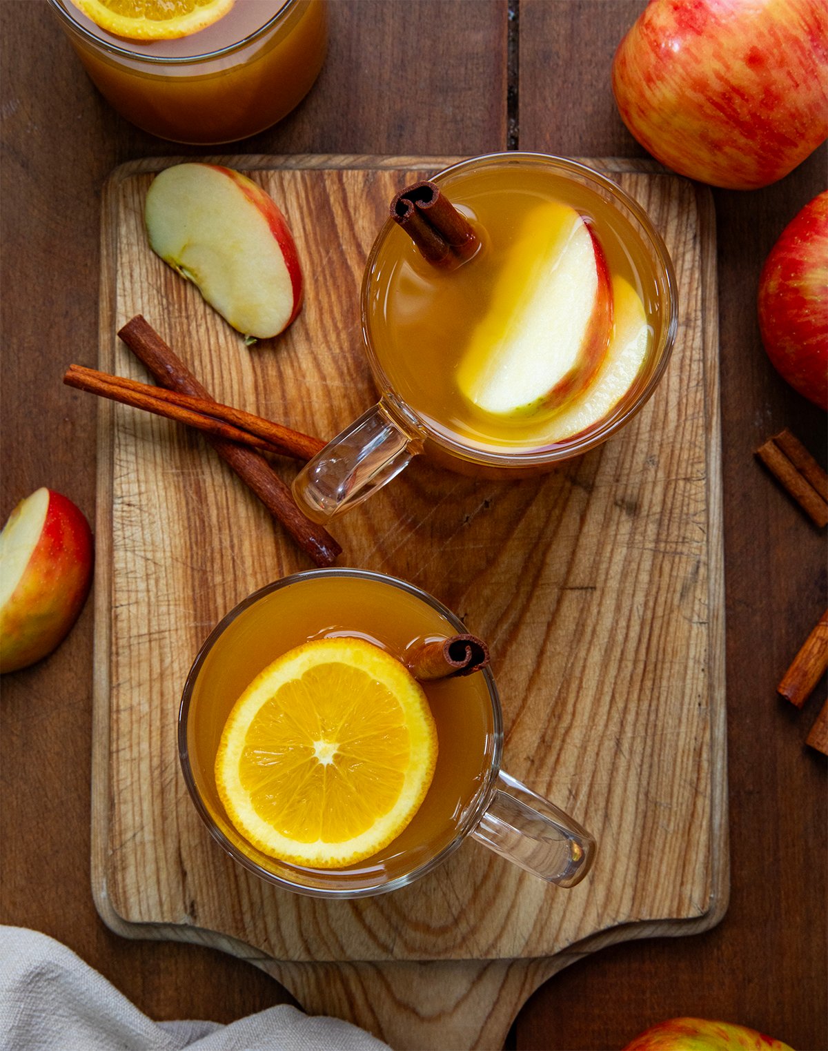 Glasses of Spiked Apple Cider on a wooden cutting board with fresh apples and cinnamon sticks from overhead.