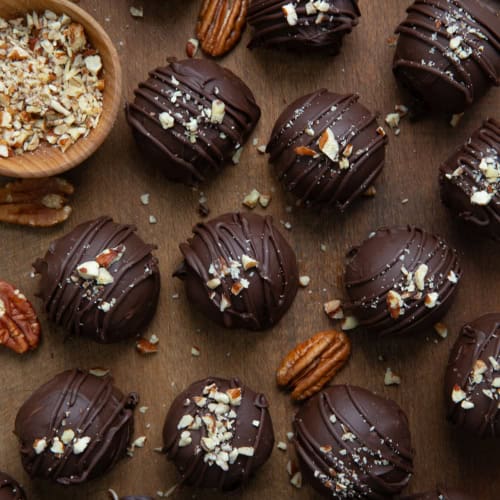 Bourbon Balls on a wooden table with whole and chopped pecans from overhead.