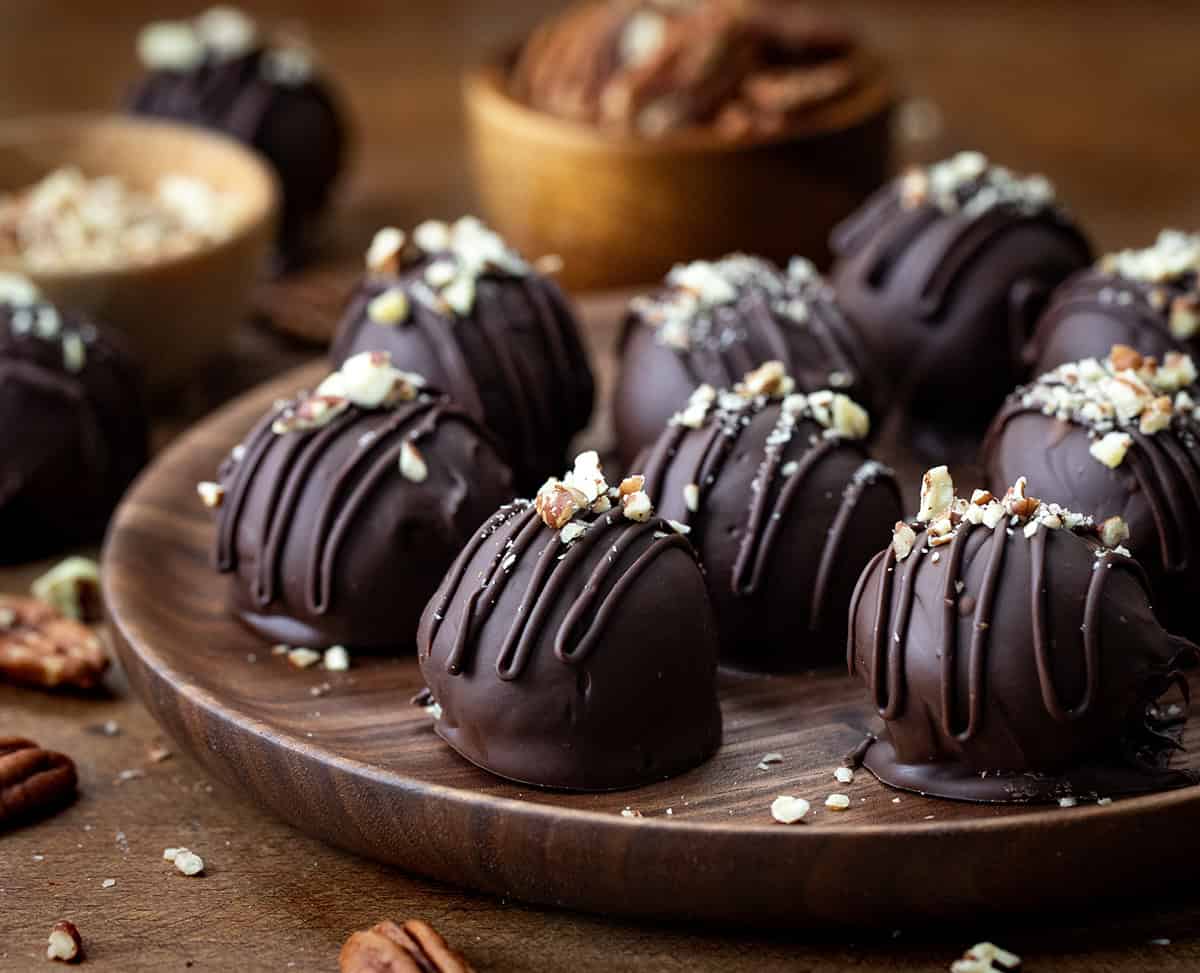 Bourbon Balls on a wooden plate on a wooden table with pecans around.