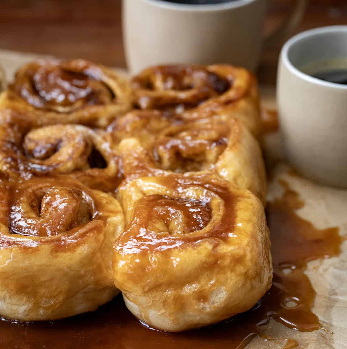 Butterscotch Caramel Rolls on parchment paper on a wooden table surrounded by ooey gooey butterscotch filling.