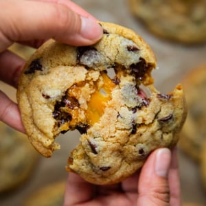 Hand breaking a Caramel Stuffed Chocolate Chip Cookie in half showing caramel inside.