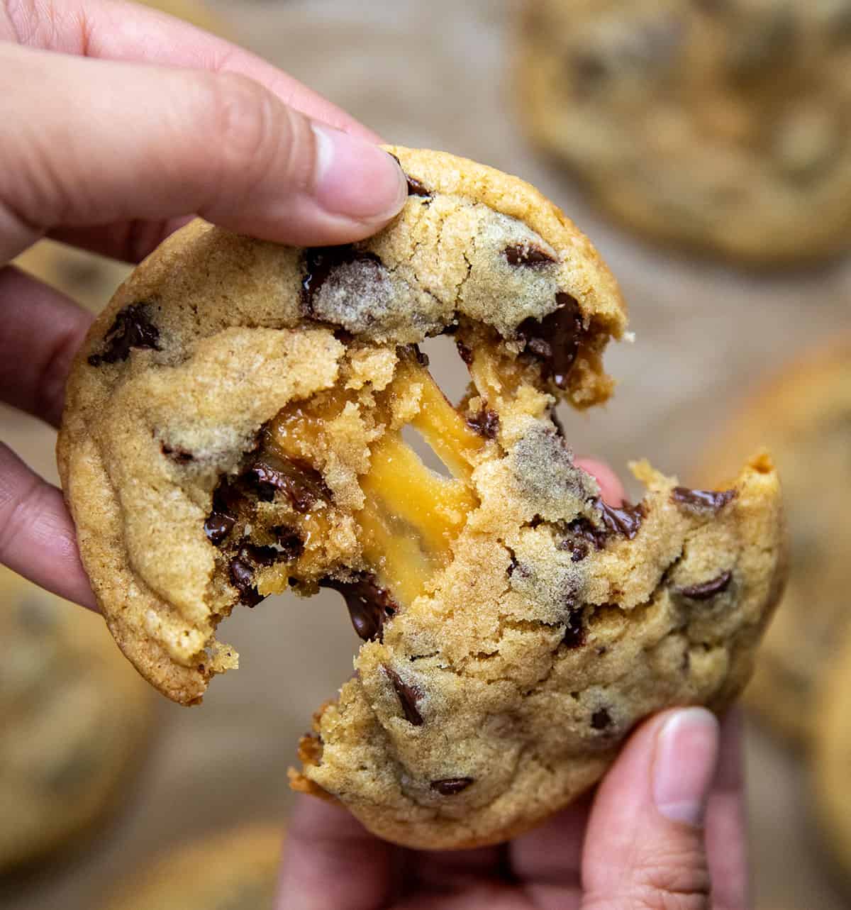 Hand breaking a Caramel Stuffed Chocolate Chip Cookie in half showing caramel inside.