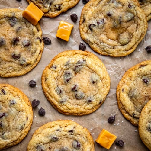 Caramel Stuffed Chocolate Chip Cookies on brown parchment paper with caramels and chocolate chips from overhead.