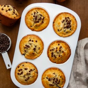 Bakery Style Chocolate Chip Muffins in a muffin pan on a wooden table from overhead.