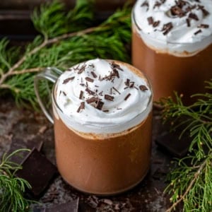 Glasses of Chocolate Eggnog on a table with evergreen and chocolate.